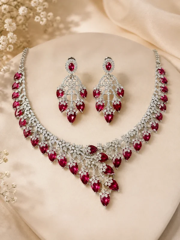 Deep Ruby Royale rhodium-plated CZ necklace set with maroon pear-shaped stones and matching earrings on a cream display