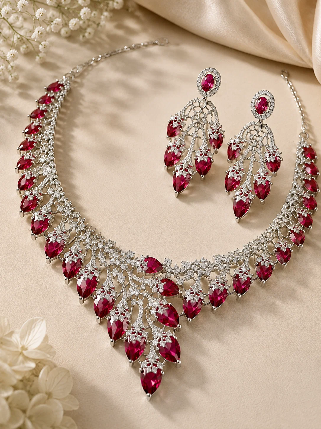 Complete Deep Ruby Royale rhodium-plated CZ necklace and earrings arranged on champagne fabric